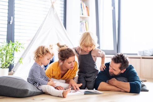 Young family with two small children indoors in bedroom reading a book. Young family with two small children indoors in bedroom reading a book.
