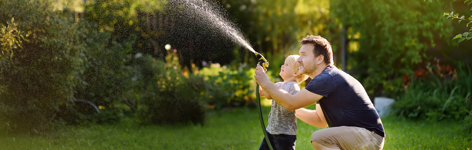 Funny little boy with his father playing with garden hose in sunny backyard Funny little boy with his father playing with garden hose in sunny backyard