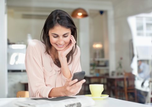 Smiling businesswoman looking down at cell phone in cafe window Smiling businesswoman looking down at cell phone in cafe window
