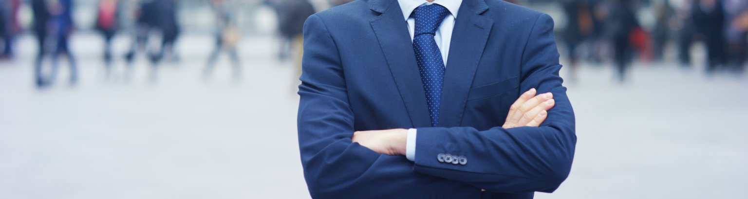 A man in a suit, looks in camera and smiles proud and sure of himself.