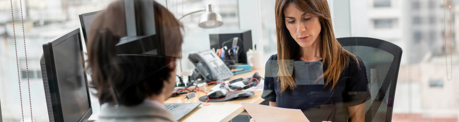 Serious female manager looking at a document while unrecognizable man is sitting at her office